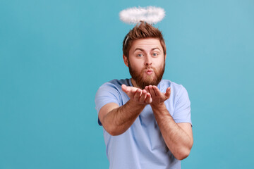 Portrait of handsome romantic young adult bearded angelic man with holy nimbus sending air kiss to...