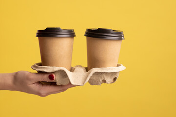 Profile side view closeup of woman hand holding and showing cup of hot takeaway mug drink in hand, coffee break at work. Indoor studio shot isolated on yellow background. - Powered by Adobe