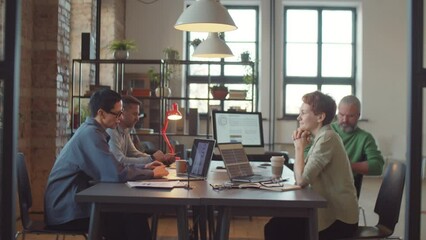 Businesswomen and businessmen using laptops and speaking while working at table in shared office space