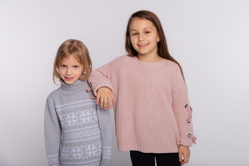 Best friends or sisters happy together stands closely each other resting hand on her friends shoulder. Smiling girls wear knitted sweaters leans at shoulder of friend