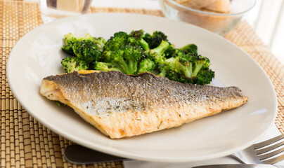 fried fillet of sea bass with garnish of broccoli on black warm stone plate