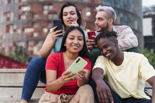 Latin and African American friends sharing social media content on smart phone. Diverse young people having fun using internet in a modern city (Barcelona)