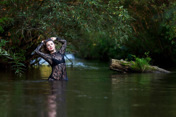 woman in a dark lace dress splashes in the river
