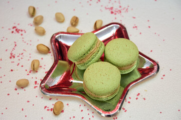 French pistachio macaroons on a plate in the form of a star. Pistachios scattered on the table