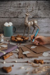 A woman's hand signs an envelope with an invitation or a postcard, a composition on a light wooden background, a vertical photo