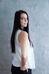 Medium vertical portrait of beautiful smiling young woman in white sleeveless top staring with a proud expression