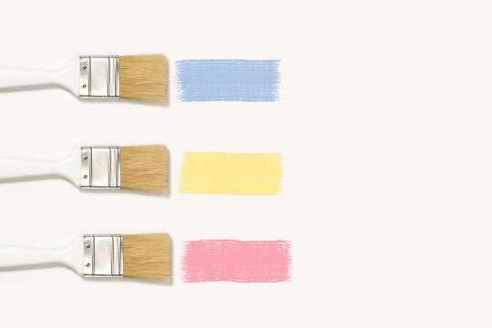 Pinceles blancos con mancha de pintura de colores rosa, amarillo y celeste sobre un fondo blanco. Vista superior y de cerca. Copy space