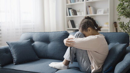 Upset teenage girl sitting on the sofa at home, feeling lonely, family problem