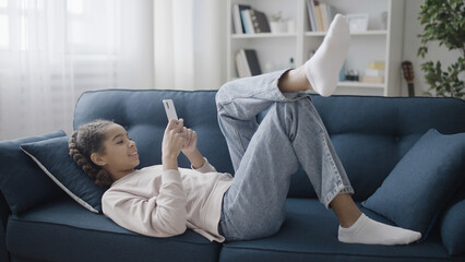 Smiling teenage girl chatting with friends online at home, using smartphone app