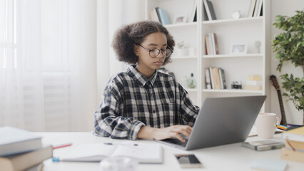 Black schoolgirl in eyeglasses doing project on laptop, online learning, school