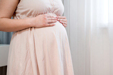 close up of pregnant woman with big belly at window.pregnancy, motherhood and expectation concept