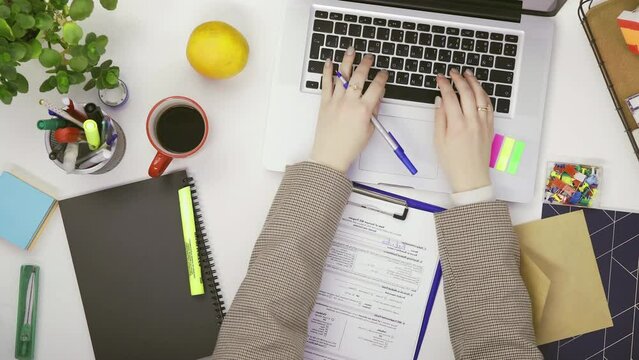 Top view of a businesswoman working at a computer and making notes on paper at a table