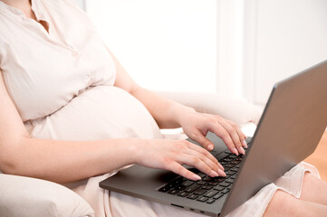 Fototapeta premium Unrecognizable pregnant woman using laptop for Browsing Internet, Shopping Online Or Reading Maternity Blog. Remote work.Online appointment with a doctor