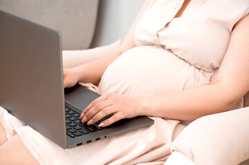 Fototapeta premium Side view on a pregnant woman using laptop for Shopping Online Or Reading Maternity Blog. Remote work.Online appointment with a doctor