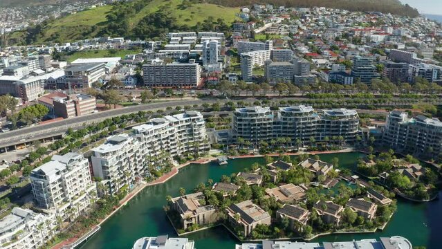 Drone footage slowly tracking sideways and looking down at the marina island and the buildings that surround it in Cape Town at high noon.