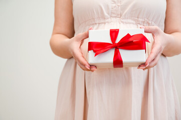 Closeup of unrecognizable pregnant woman holding gift with red ribbon.Mother's day,valentine's,baby shower concept