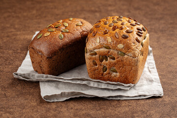 Fresh baked loaves of bread with pumpkin seeds on brown background