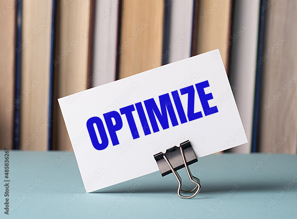 Poster a white card with the text optimize stands on a clip for papers on the table against the background 