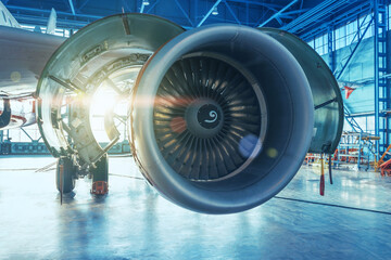 Jet engine with open hood covers on maintenance, illuminated by bright light from behind the hangar gate.