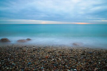 Fototapeta na wymiar Amanecer en la playa con muchas piedrecitas en la orilla del mar