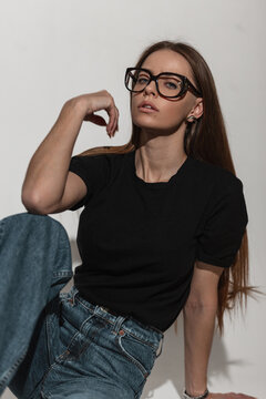 Sexy Glamorous Beauty Woman With Cool Glasses In Fashion Black Shirt Mock-up And Jeans Sits In Studio On A White Background. Pretty Lovely Girl In Fashionable Summer Clothes