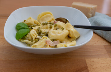 Tortellini alla panna, Tortellini with parmesan, basil, pea and boiled ham in a white plate with a spoon, focus on foreground