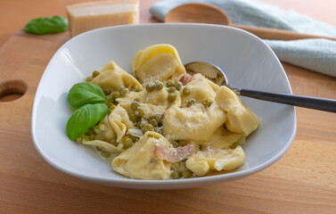 Tortellini alla panna, Tortellini with parmesan, basil, pea and boiled ham in a white plate with a spoon, focus on foreground