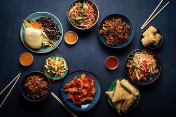 Set of Chinese dishes on table: sweet and sour chicken, fried spring rolls, noodles, rice, steamed buns with bbq glazed pork, Asian style banquet or buffet, top view with copy space
