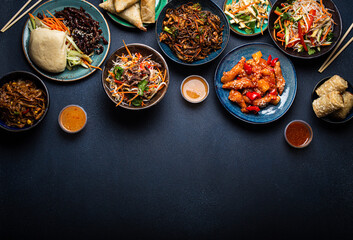 Set of Chinese dishes on table: sweet and sour chicken, fried spring rolls, noodles, rice, steamed buns with bbq glazed pork, Asian style banquet or buffet, top view with copy space
