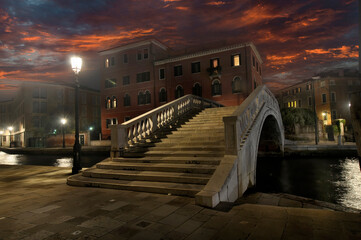 Hermosa vista nocturna de un artístico puente sobre un canal en Venecia tenuemente iluminado por...