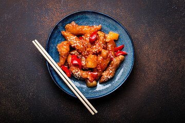 Chinese traditional wok dish sweet and sour deep fried chicken with vegetables stir-fry on plate with sesame seeds on rustic dark concrete background top view, Asian meal with chopsticks copy space
