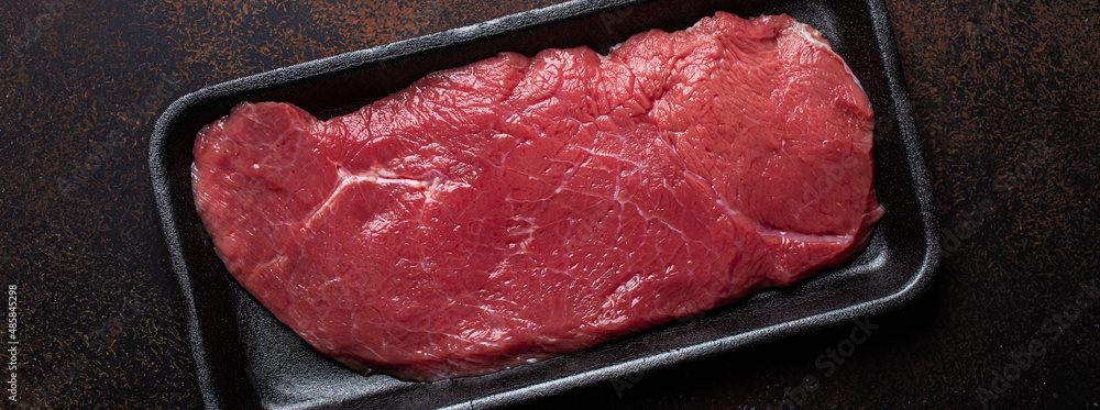 Wall mural Beef lean raw fillet steak in black plastic container on dark brown rustic concrete background from above flat lay, diet beef meat steak ready to be cooked