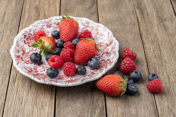 Raspberries, strawberries and blueberries on a plate over wooden table