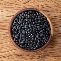 Raw black beans in a bowl over wooden table