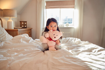 Fototapeta na wymiar Young Girl Sitting On Bed Wearing Pyjamas At Home Cuddling Soft Toy
