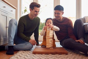 Family With Two Dads Playing Game With Daughter At Home Stacking Wooden Bricks Into Tower