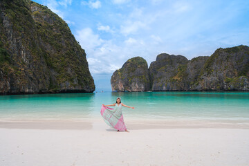 happy Asian woman tourist relax fun with a beautiful landscape view of Maya bay beach at Phi Phi Leh islands famous place in Krabi, Thailand. white sand and clear turquoise sea with cliffs in ocean.  