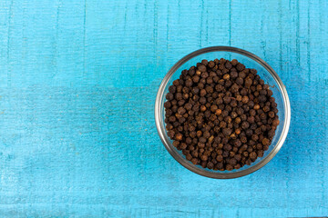 Black pepper in transparent glass bowl on blue wooden background. Black pepper is a spicy seasoning and herb for healthy.