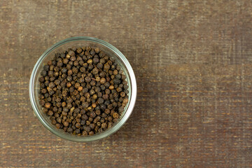 Black pepper in transparent glass bowl on brown wooden background. Black pepper is a spicy seasoning and herb for healthy.