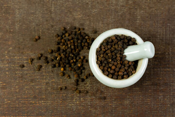 Black pepper in white mortar and pestle on wooden background top view. Black pepper is a spicy...