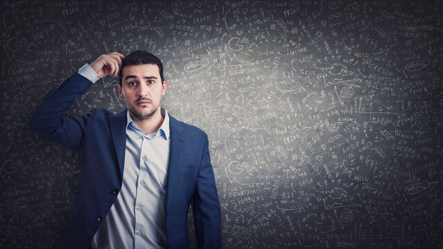 Clueless and pensive businessman scratching his head thinking for solutions on solving difficult calculations. Puzzled male looks confused in front of a blackboard with sophisticated equations