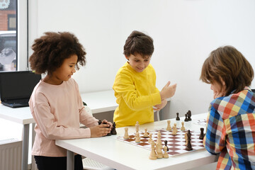 Diverse Group of kids playing chess. Concentrated multiethnic clever children with board game...