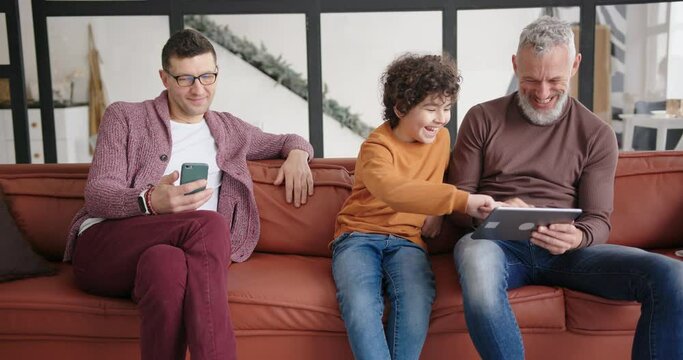 Happy gay LGBT family looks at funny photos on tablet laughing