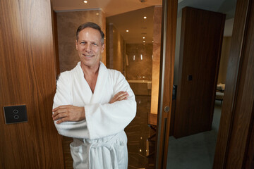 Pleasant man in cozy bathrobe posing for camera at hotel