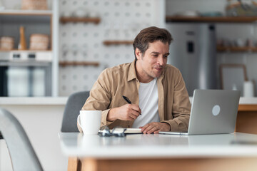 Middle-aged man taking a notes while following an online course.