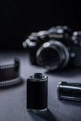 Film photography - a vintage metallic film cartridge and 35mm SLR camera against a dark background.