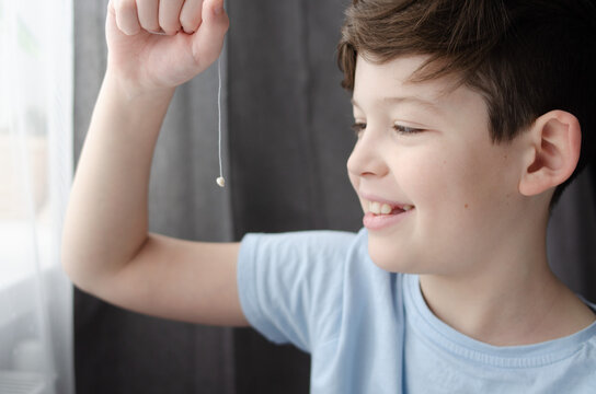 A cute boy of ten years old, holding his baby tooth on a string.