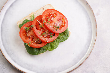 Simple and tasty vegan sandwich with white wheat toast bread, slices of tomato, spinach and microgreens on scandi plate on light grey background