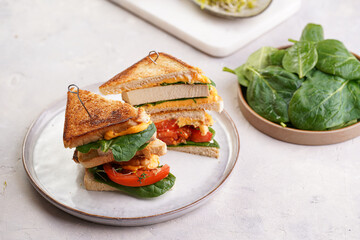 American homemade tall hot grilled cheese sandwich with tofu, cheddar, tomato slices and spinach on...