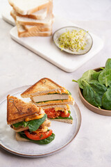 American homemade tall hot grilled cheese sandwich with tofu, cheddar, tomato slices and spinach on white scandi plate cut in triangles. Italian Tramezzini